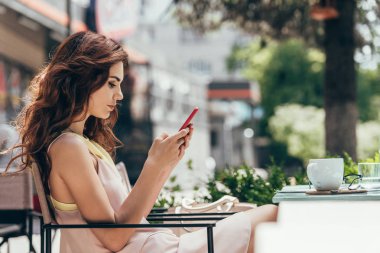 kafede kahve ile masada otururken smartphone kullanan genç kadın yan görünüm