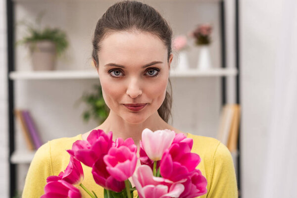 beautiful adult woman holding pink tulips bouquet and looking at camera