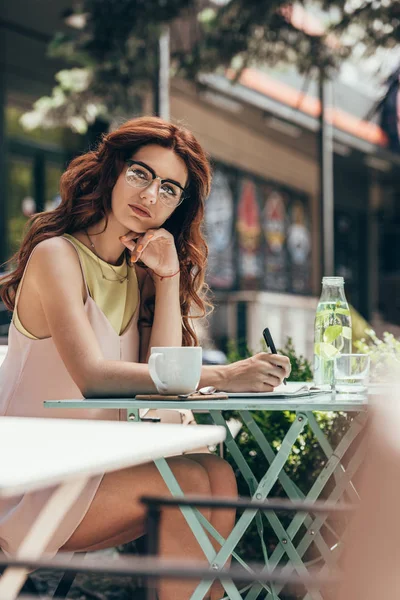 Nachdenkliche Geschäftsfrau Mit Brille Sitzt Mit Notizbuch Und Kaffeetasse Tisch — Stockfoto