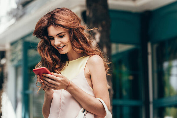portrait of young stylish woman using smartphone on street