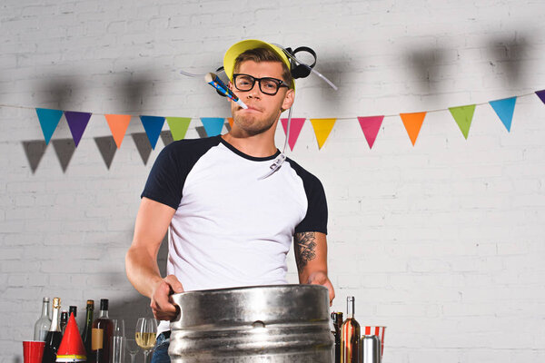 handsome young man in beer hat holding keg of beer and smiling at camera