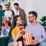 Junger Mann und Frau schauen einander beim Bier trinken und Popcorn essen auf der Heimparty an