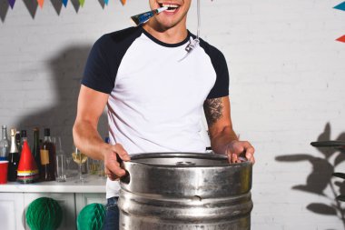 cropped shot of happy young man holding barrel of beer at home party clipart