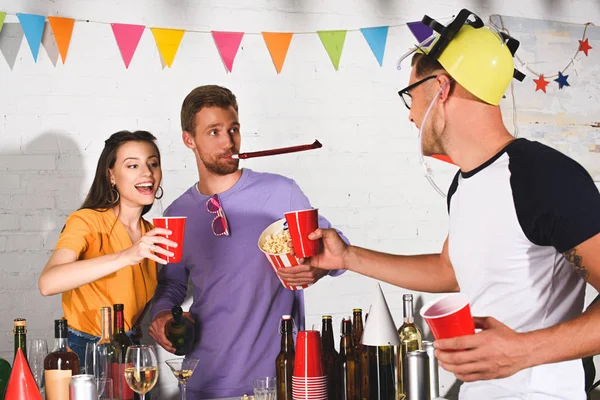 happy young people drinking alcohol and eating popcorn at home party