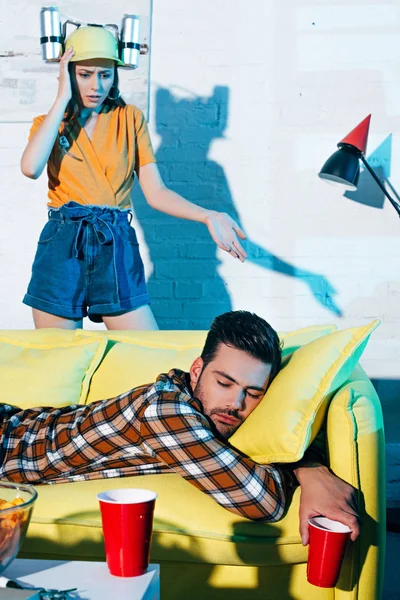 Shocked Girl Beer Hat Looking Drunk Man Sleeping Couch Home — Stock Photo, Image