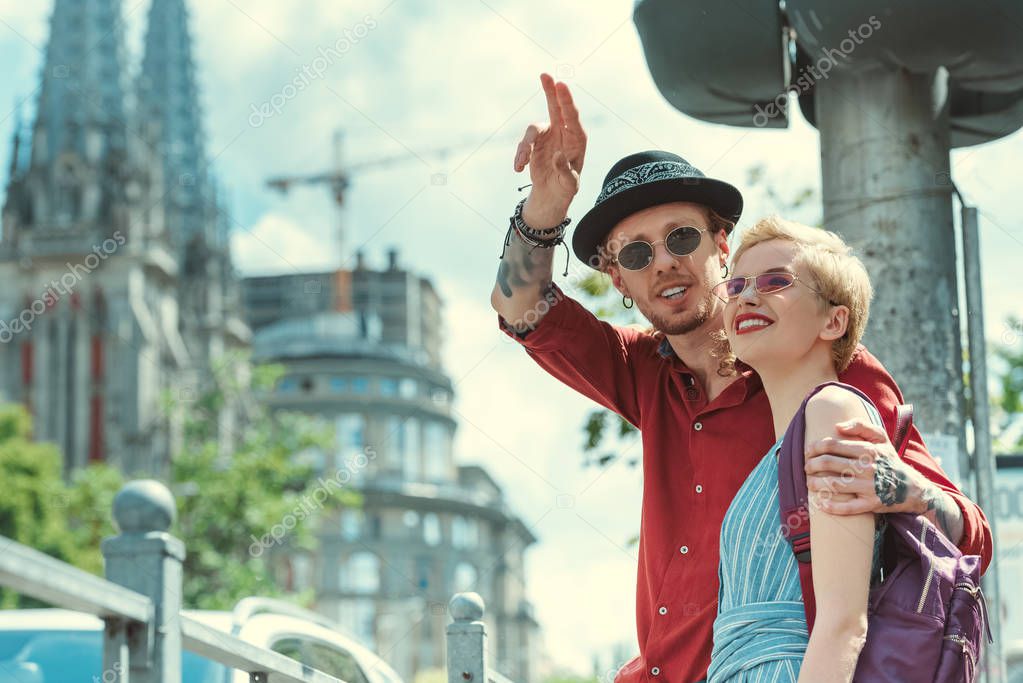 smiling stylish couple of tourists pointing at something in city