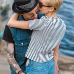 Boyfriend with tattoos and stylish girlfriend hugging and leaning on railing near river