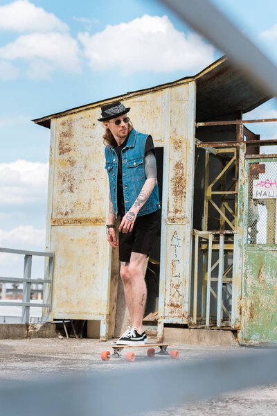 handsome stylish tattooed skater standing on longboard