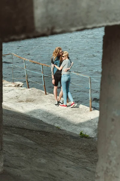 纹身男友和时尚女友拥抱在河边的桥上 — 免费的图库照片