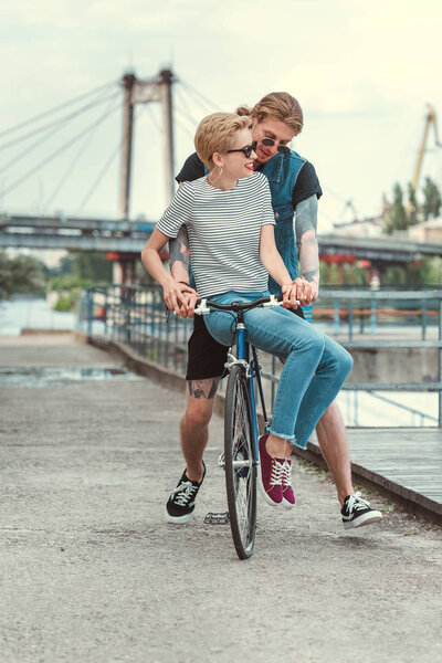 boyfriend with tattoos and smiling stylish girlfriend on bicycle on bridge