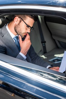 düşünceli genç işadamı araba arka üzerinde koltuk belgeleriyle çalışma