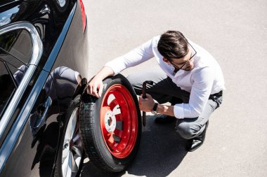 high angle view of young businessman replacing wheel of car at street clipart
