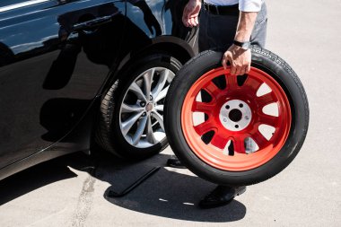 cropped image of businessman holding tire for wheel replacement at street clipart