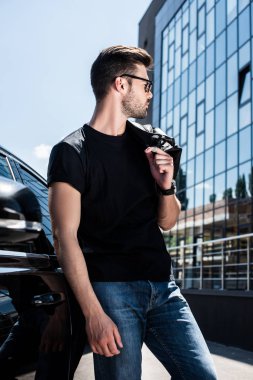 omuz Street car yakınındaki deri ceket tutan güneş gözlüğü şık adam yan görünüm