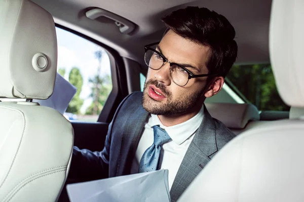 Wütender Junger Geschäftsmann Mit Brille Und Dokumenten Auf Dem Rücksitz — kostenloses Stockfoto