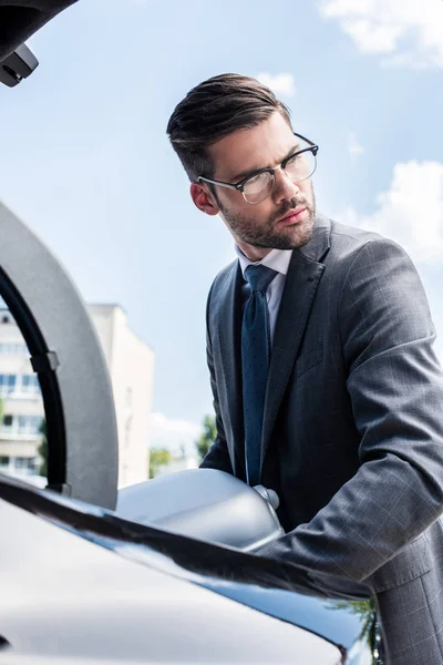 Affärsman Glasögon Tittar Bort Och Sätta Hjulförsedda Väska Bilen Stammen — Stockfoto