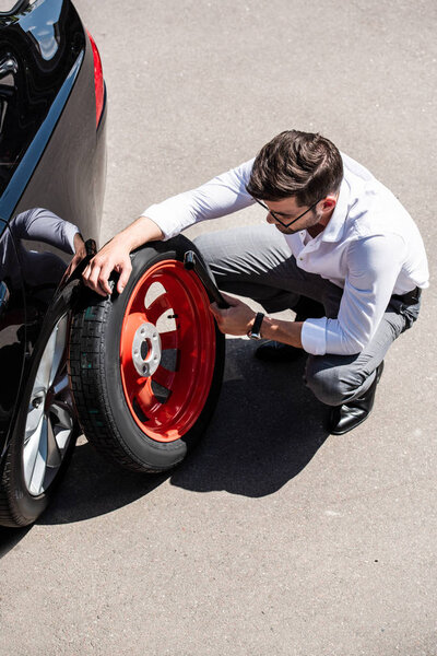 high angle view of businessman in eyeglasses holding tool for wheel replacement at street