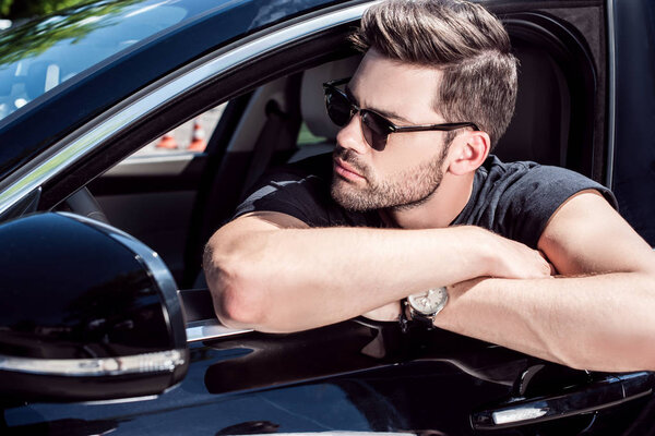 портрет серьезного стильного мужчины в солнцезащитных очках, смотрящего в сторону, сидя в машине
 