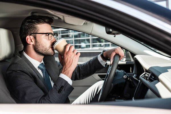 side view of businessman in eyeglasses drinking coffee and riding car 