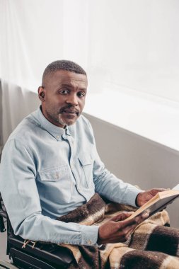 kitap ve kameraya bakarak tekerlekli sandalye Engelli kıdemli insanın yüksek açılı görünüş