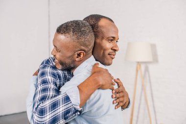 happy senior father and smiling adult son hugging at home  clipart