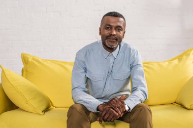 sarı kanepede oturan ve kameraya gülümseyen kıdemli Afrikalı-Amerikalı adam