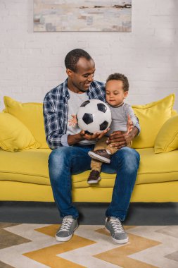 happy young father holding soccer ball and looking at cute smiling son clipart