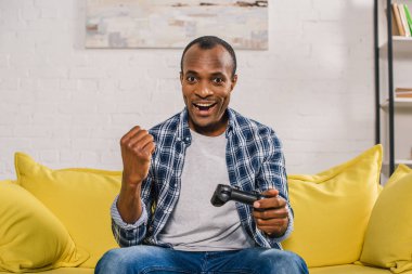 joystick ile evde oynarken kameraya gülümseyen neşeli Afrikalı-Amerikalı adam