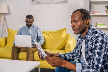 Genç adam gazete ve üst düzey baba arkasında dizüstü kullanarak okuma