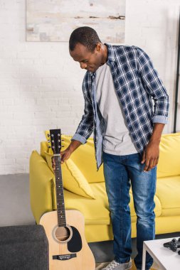 Akustik gitar evde tutan genç Afro-Amerikan adam