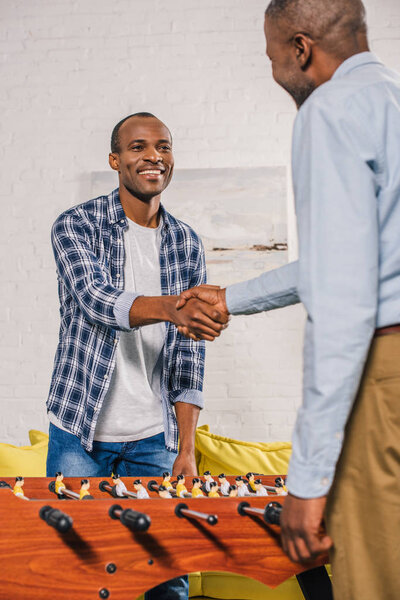 senior father and adult son shaking hands while playing table football at home