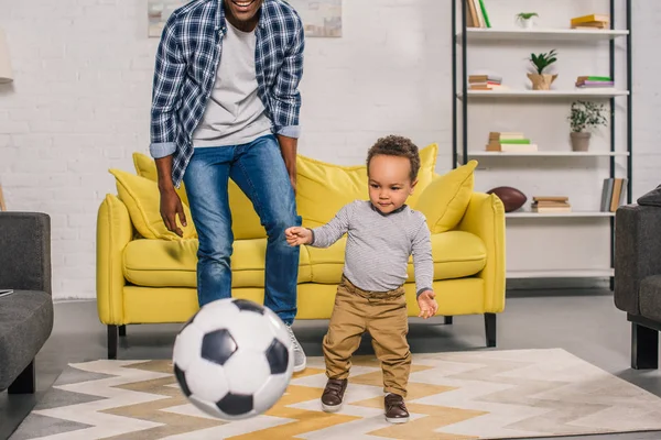 cropped shot of smiling father with cute little son playing with soccer ball at home
