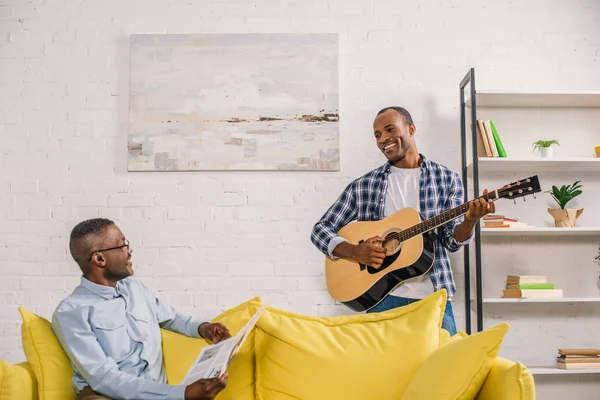 gazete ve gülümseyen Yetişkin oğlu evde birbirine bakarak gitar ile mutlu komuta sizde 