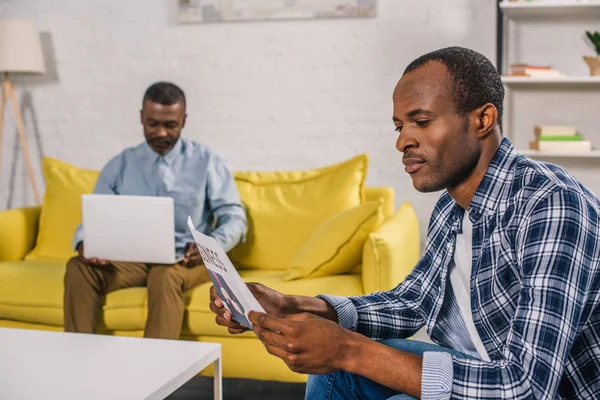Genç adam gazete ve üst düzey baba arkasında dizüstü kullanarak okuma