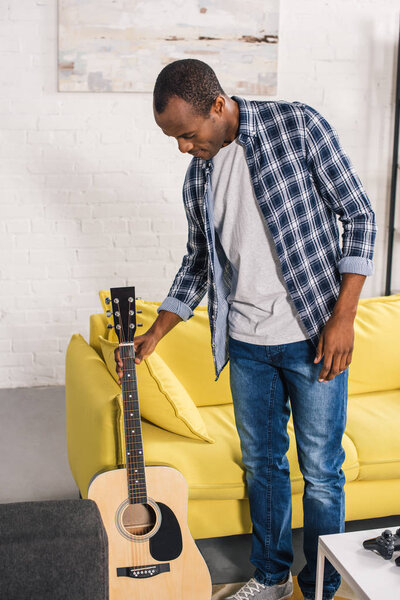 young african american man holding acoustic guitar at home
