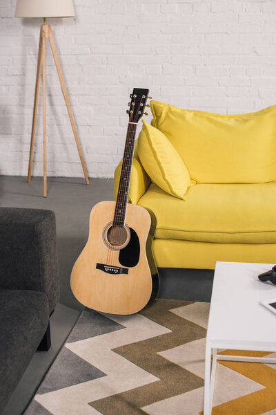 acoustic guitar near cozy yellow couch in modern interior