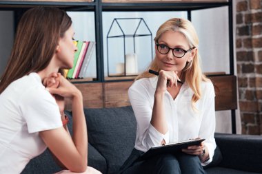 smiling female counselor with clipboard listening to patient at office  clipart