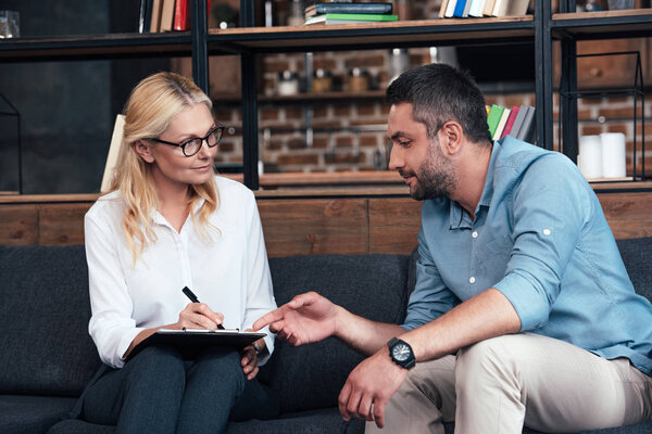 man pointing by finger on clipboard of female counselor at office 