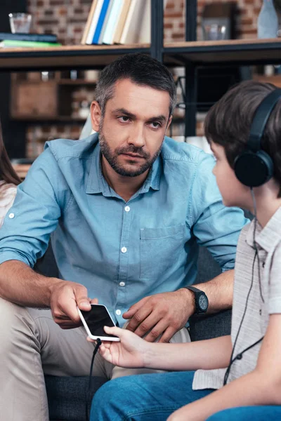 Poważne Ojciec Zabierając Smartphone Synka Słuchawkach — Darmowe zdjęcie stockowe