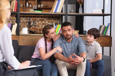 children cheering up father while he talking to female counselor on therapy session  clipart