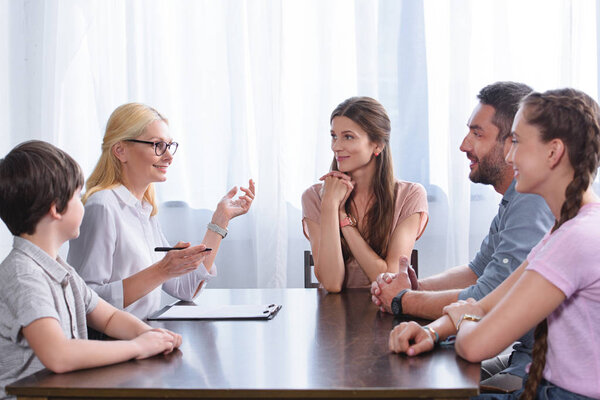 female counselor gesturing by hand and talking to family on therapy session in office 