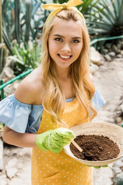 toprak bir kase tutarak ve sera kameraya gülümseyen güzel sarışın kızın yüksek açılı görünüş 