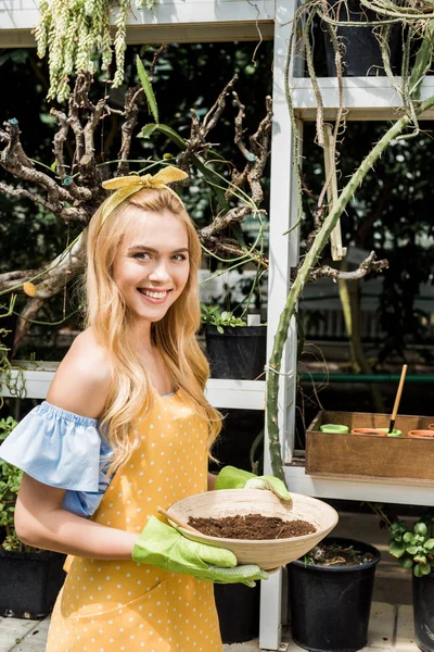 Hermosa Mujer Joven Sosteniendo Tazón Con Tierra Sonriendo Cámara Invernadero — Foto de stock gratis