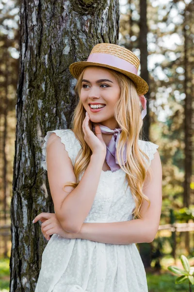 ağacın yanında duran ve uzağa arıyorsunuz kurdele ile hasır şapkalı güzel sarışın kız