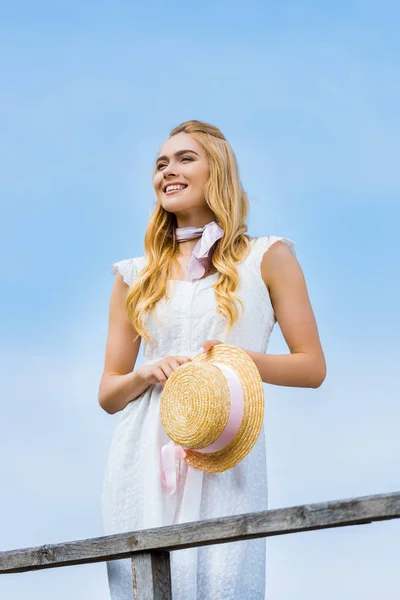 Beautiful Smiling Blonde Girl Holding Wicker Hat Ribbon Looking Away — Stock Photo, Image