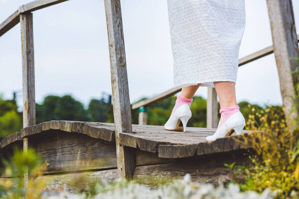 cropped shot of woman in white dress walking on wooden footbridge 