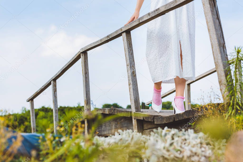 low section of girl in white dress walking on wooden footbridge 