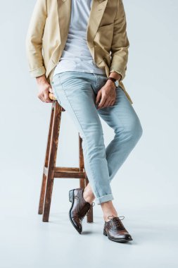 Beyaz arka plan taburede oturan şık genç adam görünümünü kırpılmış