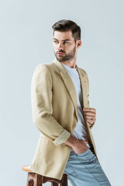 Taburede oturan ve dış saha üzerinde izole beyaz arka plan seyir yakışıklı sakallı adam