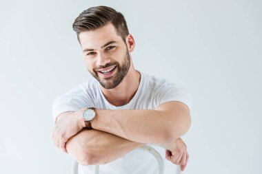 Sandalye üzerinde oturan beyaz arka plan üzerinde izole iken gülümseyen moda kendine güvenen adam